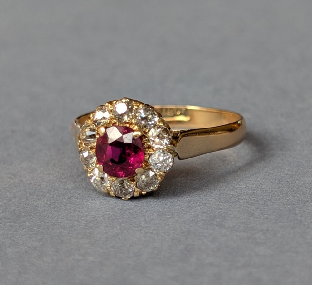 An antique 18ct gold cluster ring featuring a central faceted red ruby surrounded by ten round diamonds. View III
