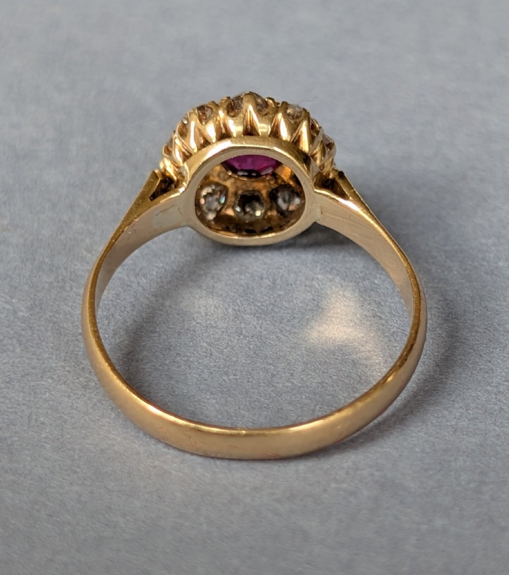 An antique 18ct gold cluster ring featuring a central faceted red ruby surrounded by ten round diamonds. View IV