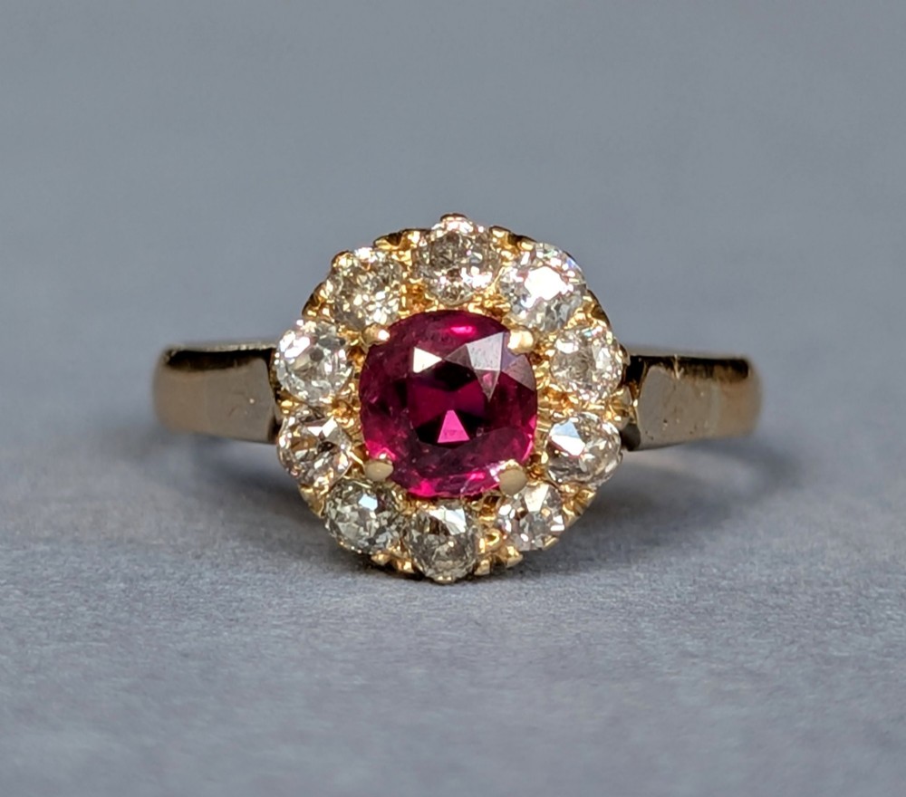 An antique 18ct gold cluster ring featuring a central faceted red ruby surrounded by ten round diamonds.