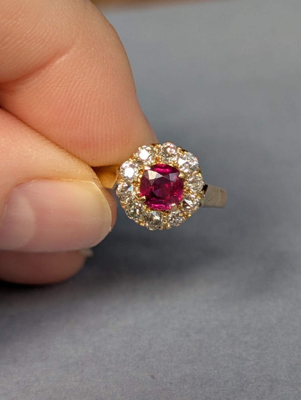 An antique 18ct gold cluster ring featuring a central faceted red ruby surrounded by ten round diamonds. View V