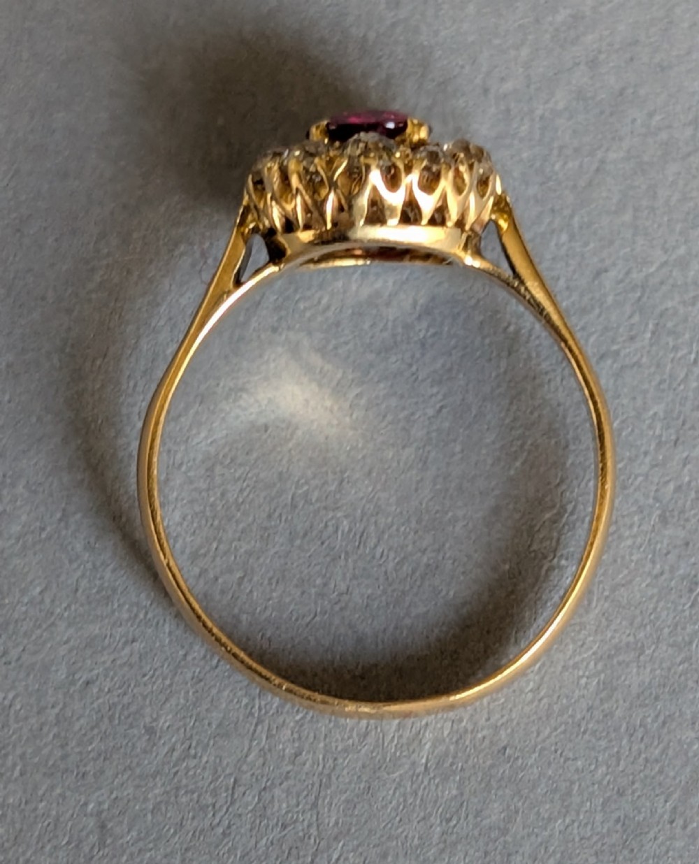 An antique 18ct gold cluster ring featuring a central faceted red ruby surrounded by ten round diamonds. View VI