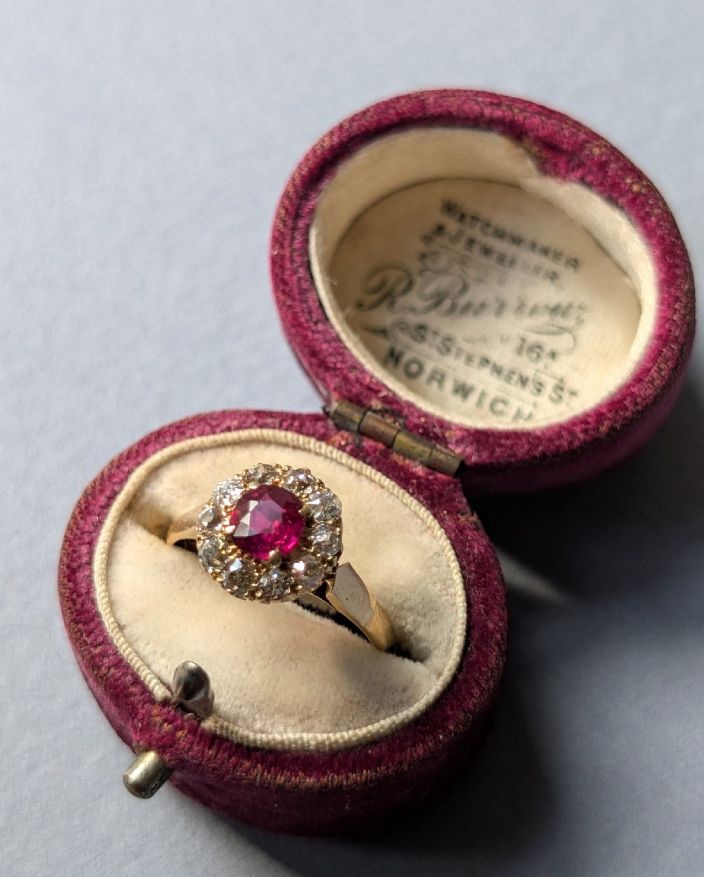 An antique 18ct gold cluster ring featuring a central faceted red ruby surrounded by ten round diamonds. View VII