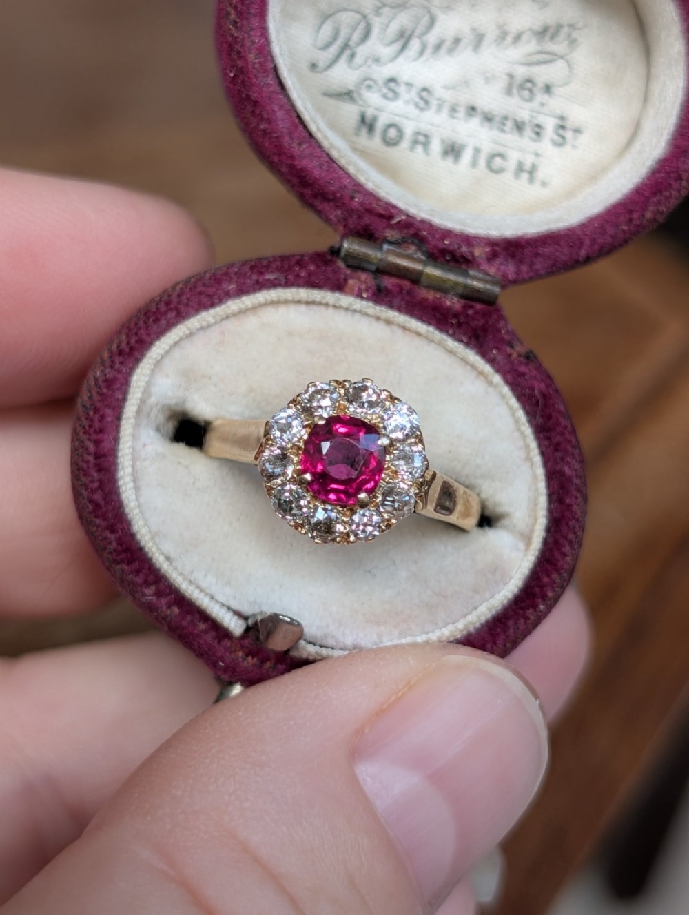 An antique 18ct gold cluster ring featuring a central faceted red ruby surrounded by ten round diamonds. View VIII