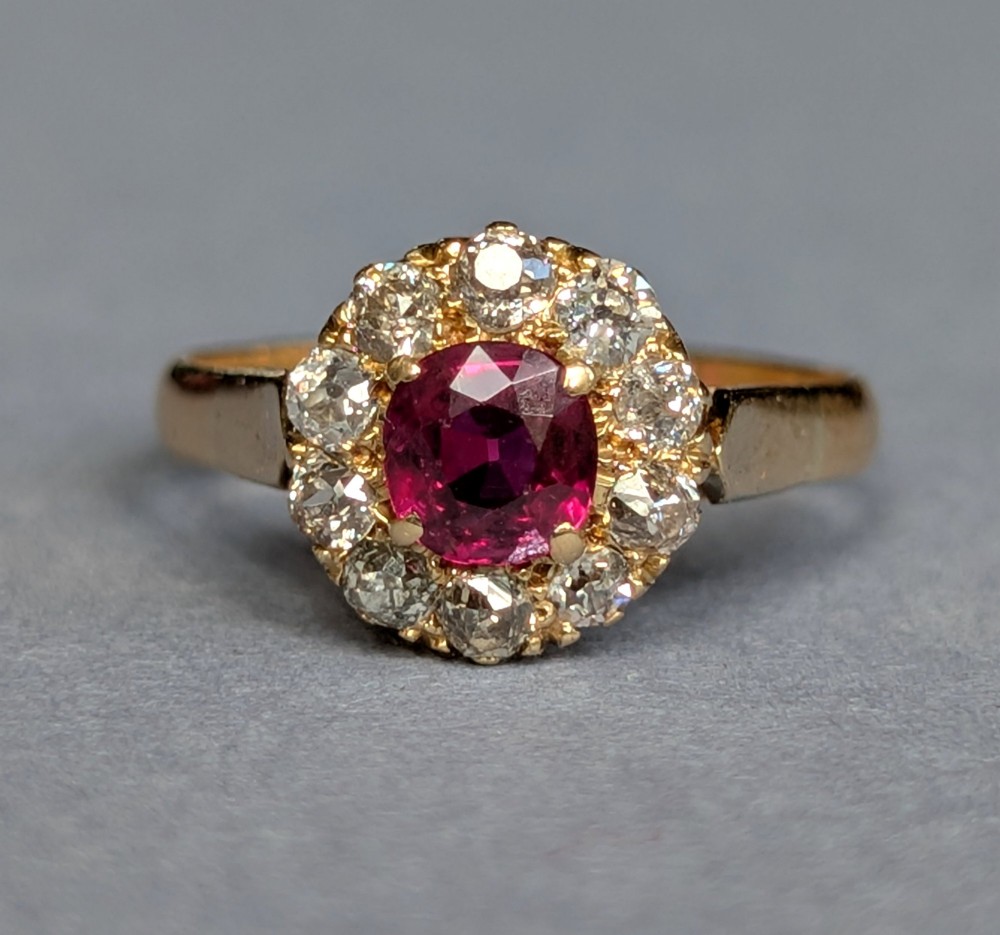 An antique 18ct gold cluster ring featuring a central faceted red ruby surrounded by ten round diamonds. View IX