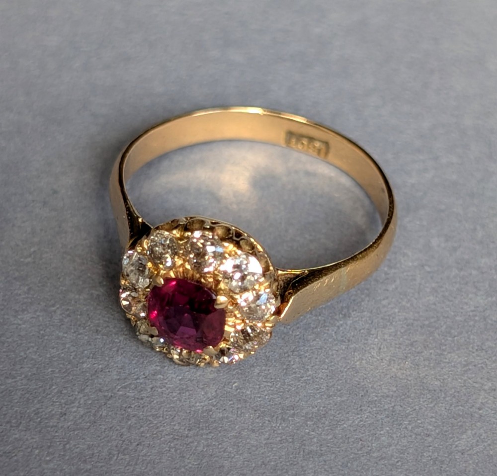 An antique 18ct gold cluster ring featuring a central faceted red ruby surrounded by ten round diamonds. View XI