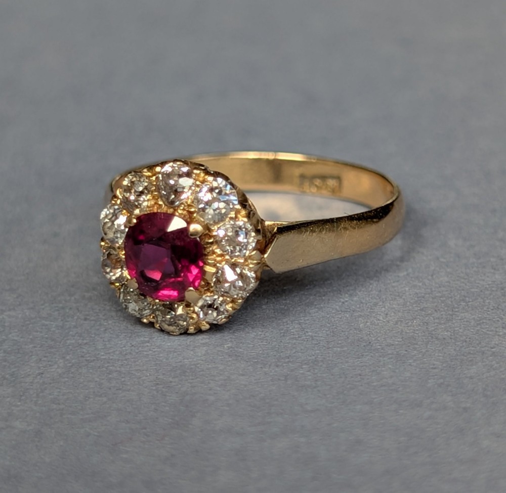 An antique 18ct gold cluster ring featuring a central faceted red ruby surrounded by ten round diamonds. View XII