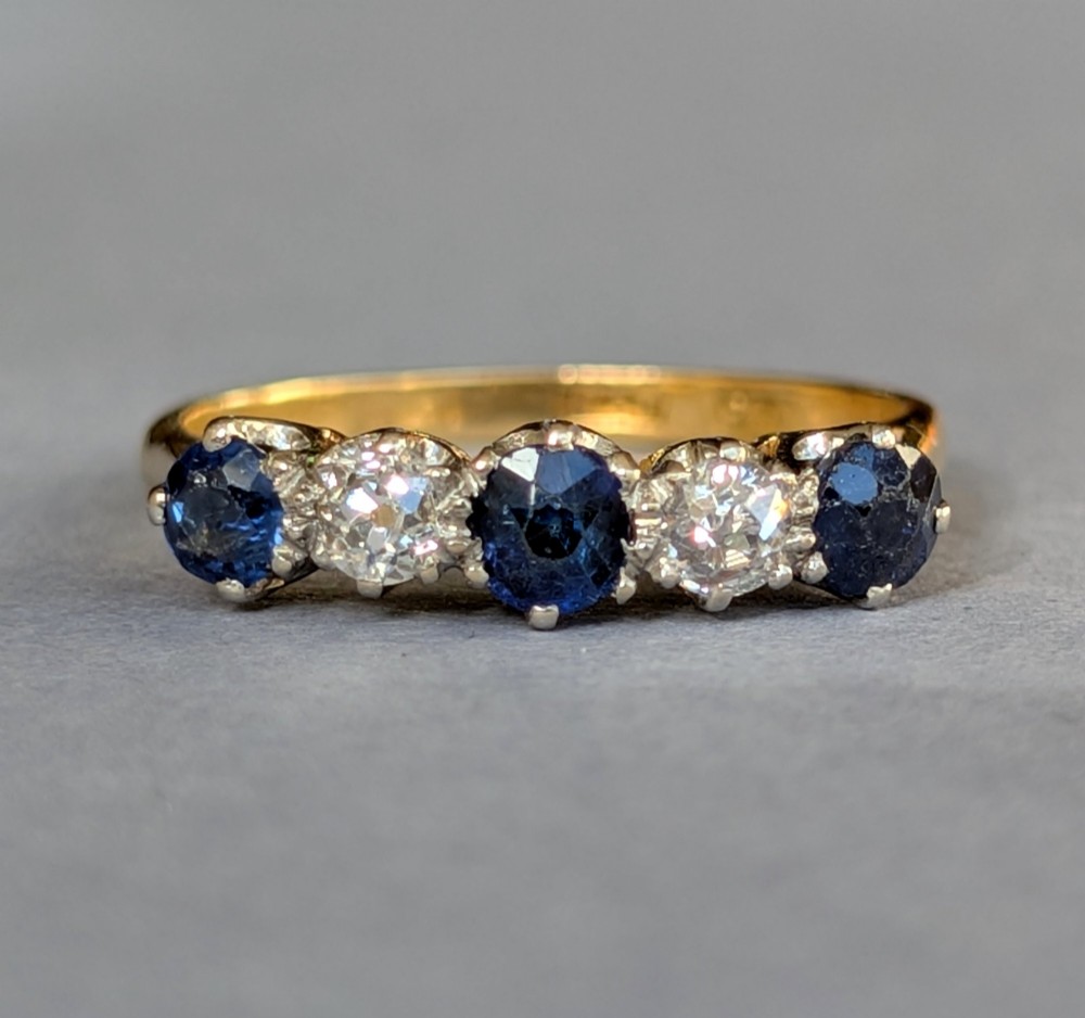 An Art Deco five-stone ring featuring three round blue sapphires alternating with two diamonds set in platinum on an 18ct yellow gold band.