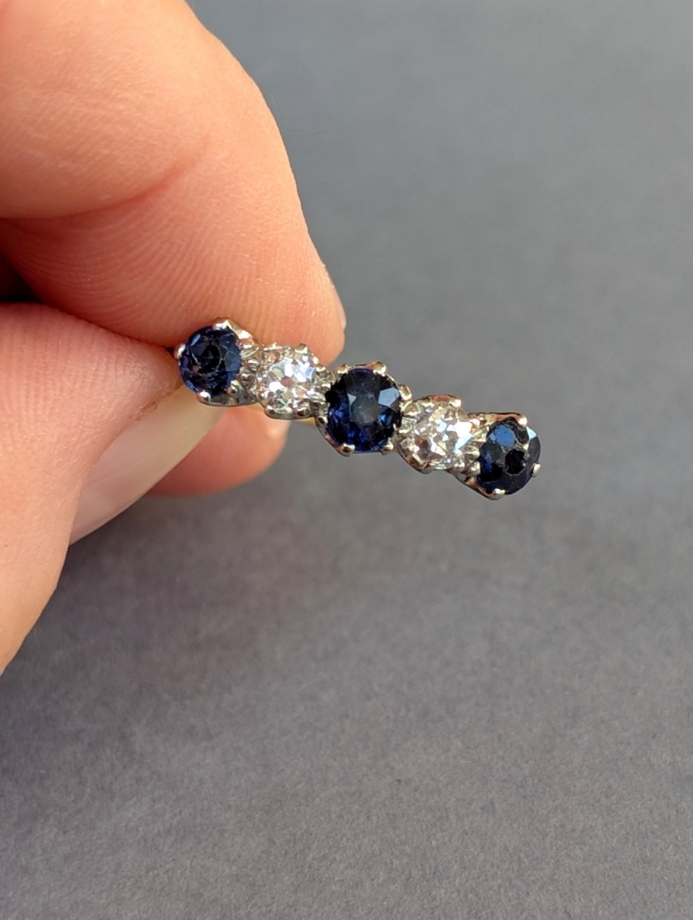 An Art Deco five-stone ring featuring three round blue sapphires alternating with two diamonds set in platinum on an 18ct yellow gold band. View II