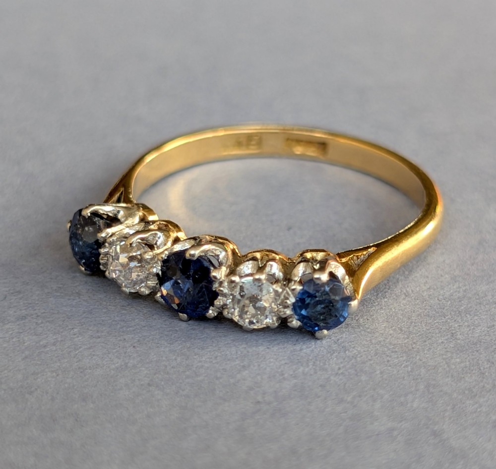 An Art Deco five-stone ring featuring three round blue sapphires alternating with two diamonds set in platinum on an 18ct yellow gold band. View III