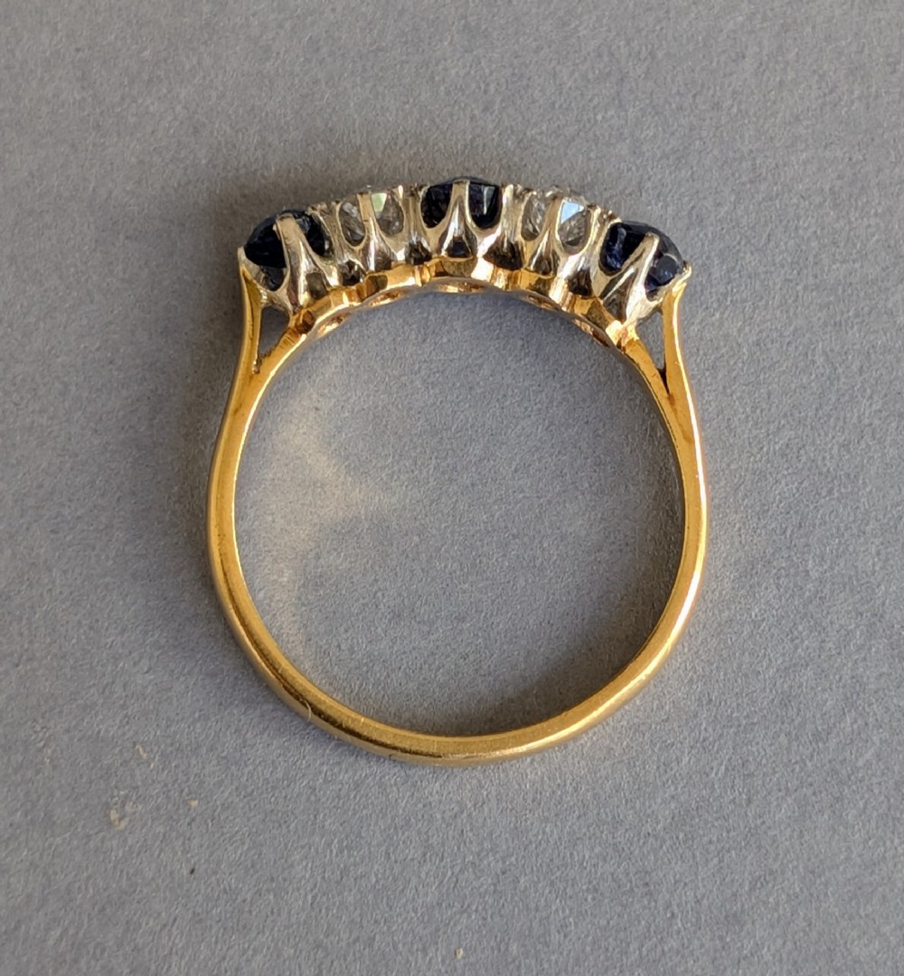 An Art Deco five-stone ring featuring three round blue sapphires alternating with two diamonds set in platinum on an 18ct yellow gold band. View IV