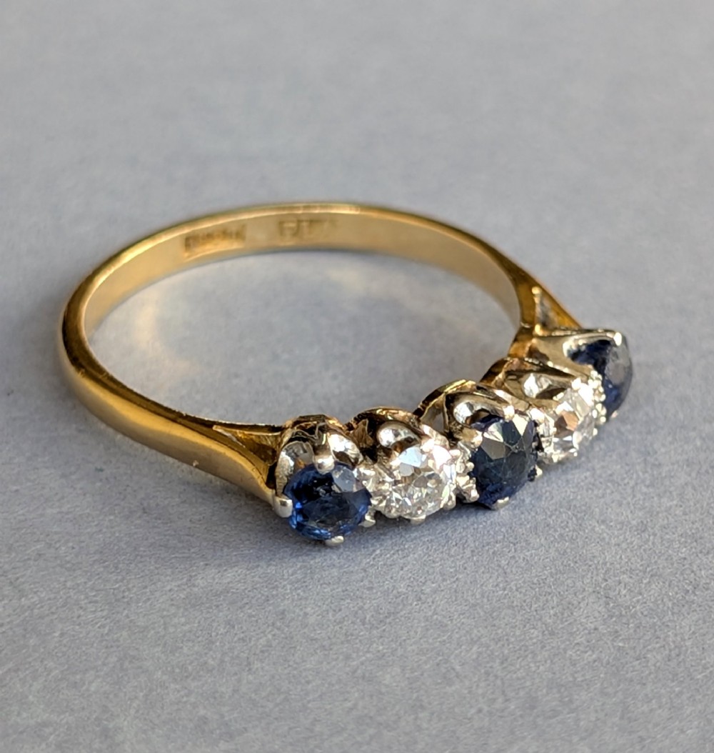 An Art Deco five-stone ring featuring three round blue sapphires alternating with two diamonds set in platinum on an 18ct yellow gold band. View VI