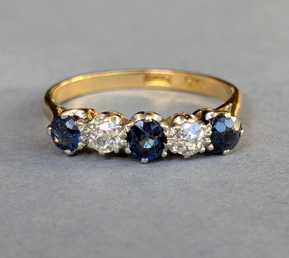 An Art Deco five-stone ring featuring three round blue sapphires alternating with two diamonds set in platinum on an 18ct yellow gold band. View VIII