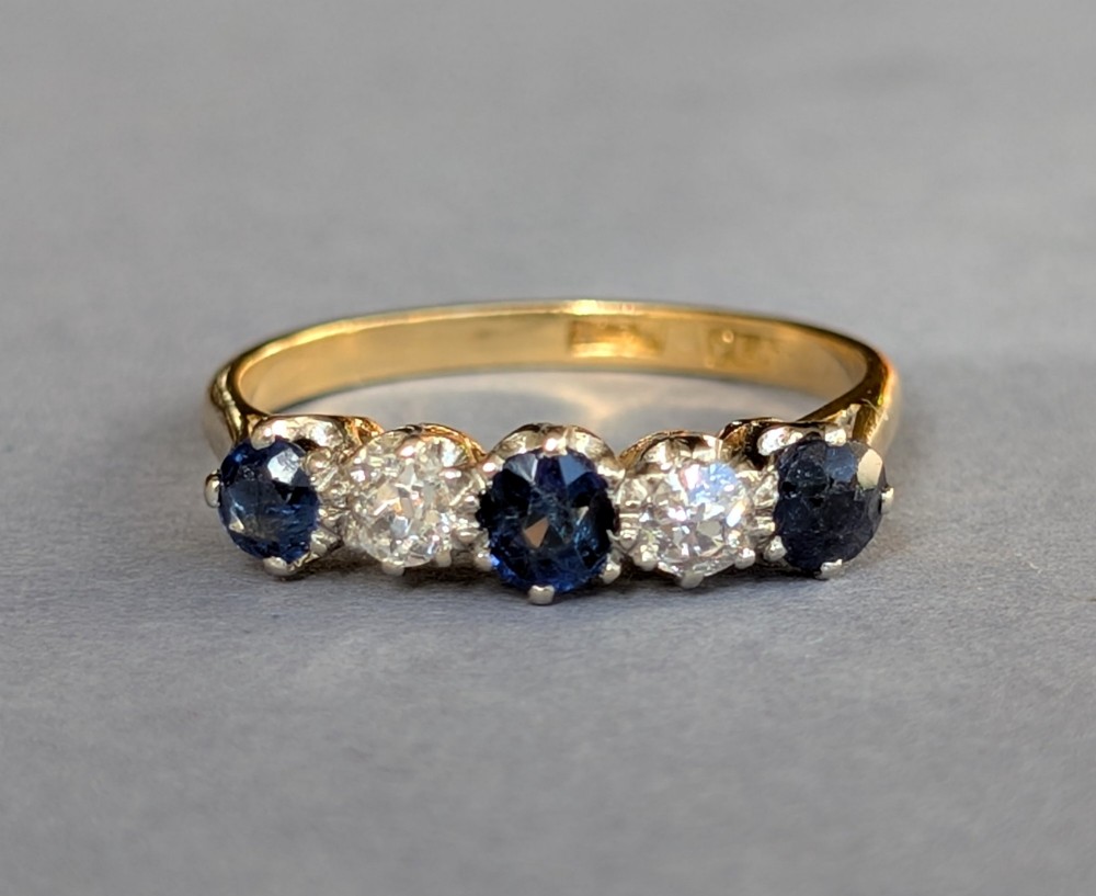 An Art Deco five-stone ring featuring three round blue sapphires alternating with two diamonds set in platinum on an 18ct yellow gold band. View IX