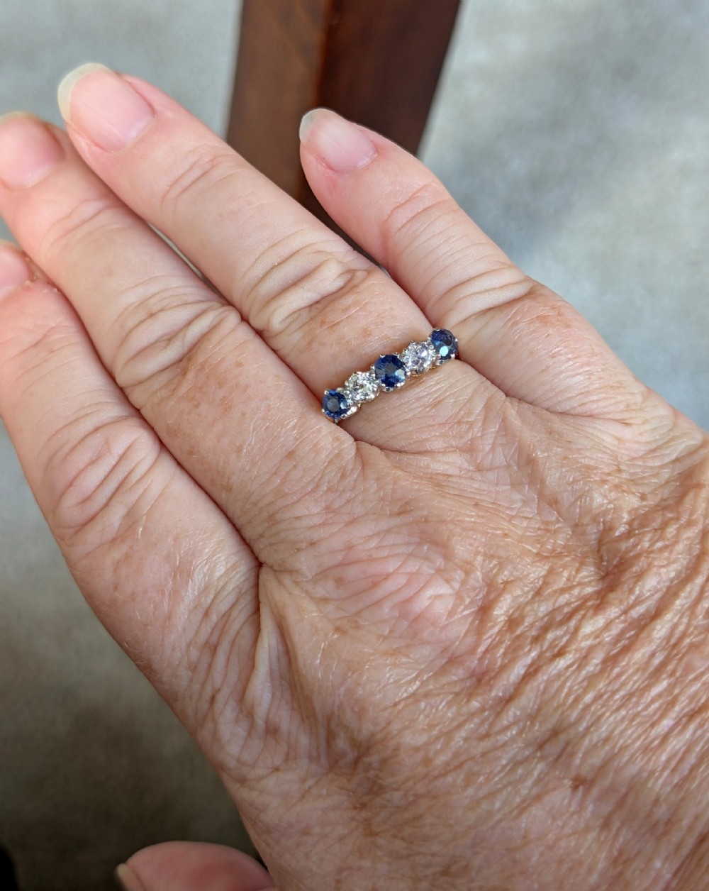 An Art Deco five-stone ring featuring three round blue sapphires alternating with two diamonds set in platinum on an 18ct yellow gold band. View X