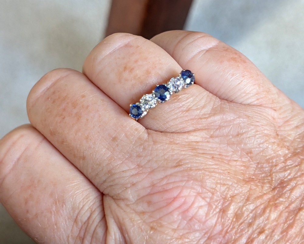 An Art Deco five-stone ring featuring three round blue sapphires alternating with two diamonds set in platinum on an 18ct yellow gold band. View XI