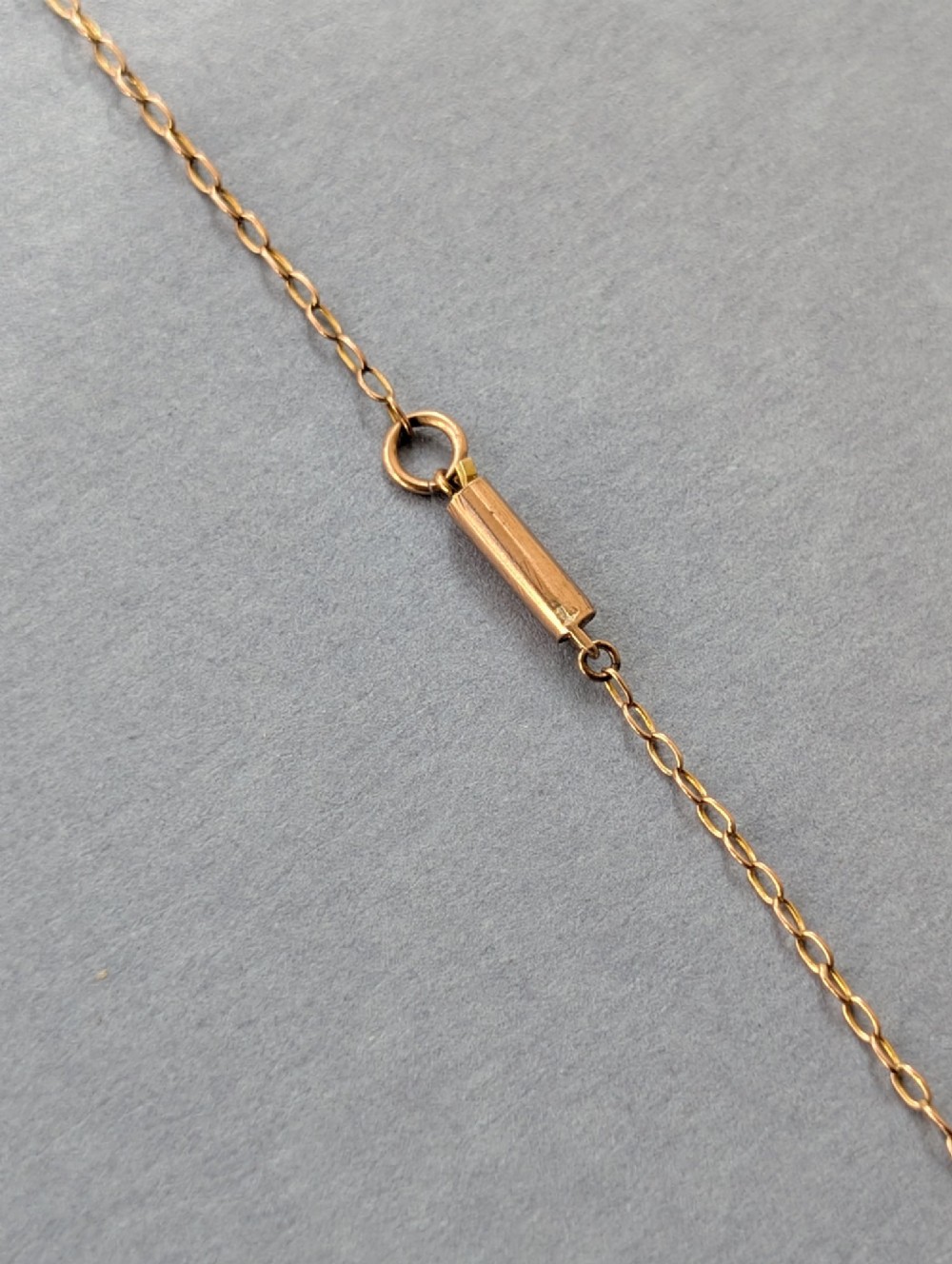 An Edwardian openwork gold lavalier pendant set with an oval purple garnet, a seed pearl center, a pearl drop, and a small green peridot, suspended from a gold chain. View VIII