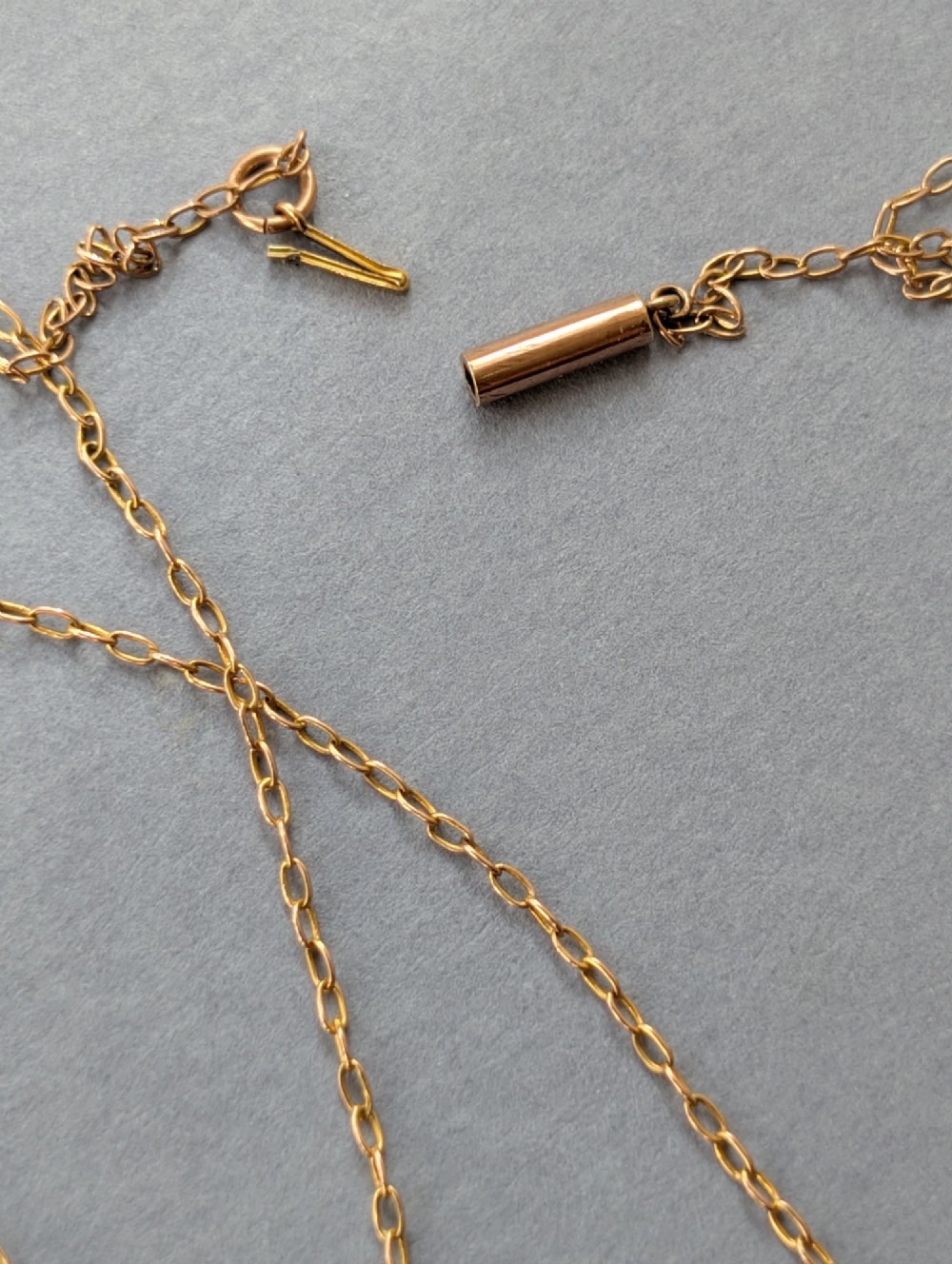 An Edwardian openwork gold lavalier pendant set with an oval purple garnet, a seed pearl center, a pearl drop, and a small green peridot, suspended from a gold chain. View IX