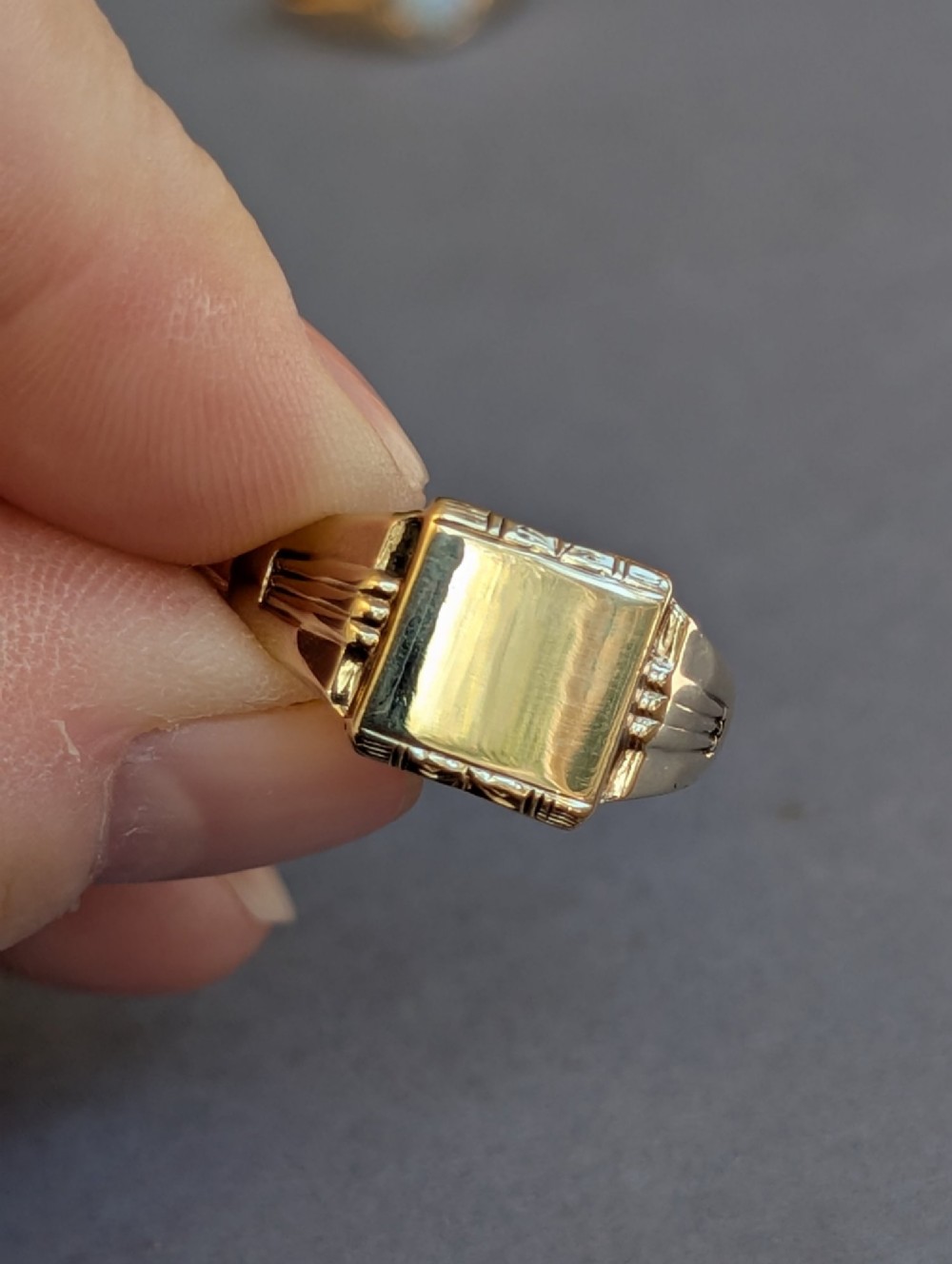 A vintage 9ct yellow gold signet ring featuring a flat square face with decorative engraved top and bottom edges and grooved shoulders. View V