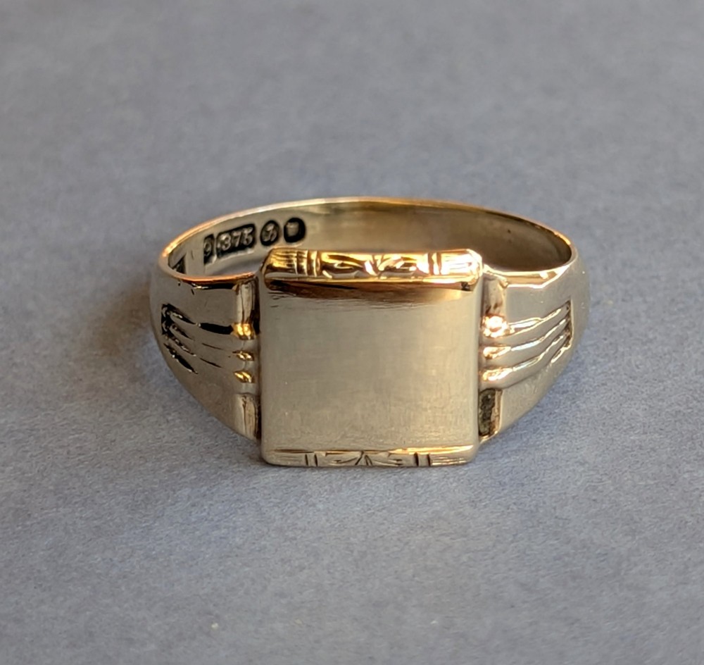 A vintage 9ct yellow gold signet ring featuring a flat square face with decorative engraved top and bottom edges and grooved shoulders. View VI