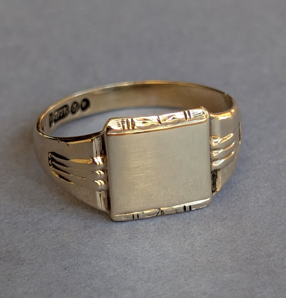A vintage 9ct yellow gold signet ring featuring a flat square face with decorative engraved top and bottom edges and grooved shoulders. View VII