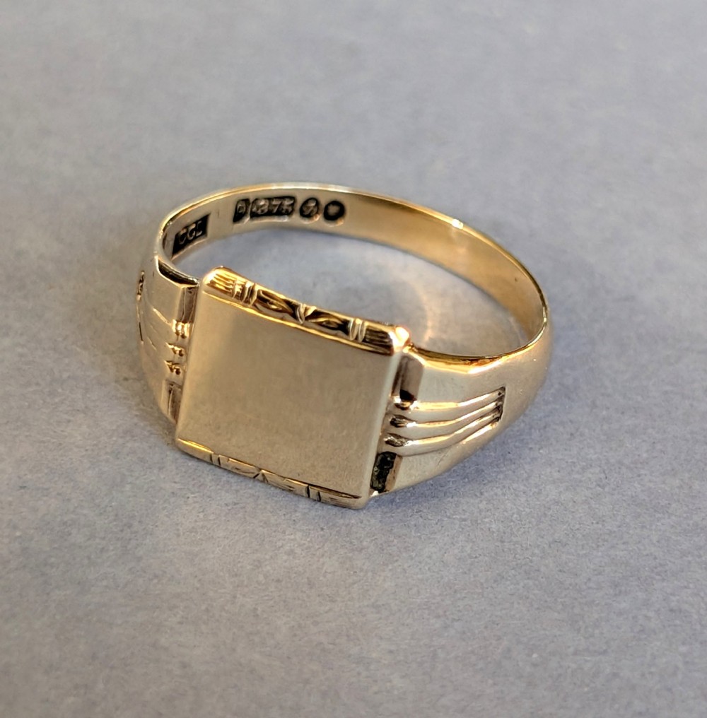 A vintage 9ct yellow gold signet ring featuring a flat square face with decorative engraved top and bottom edges and grooved shoulders. View IX