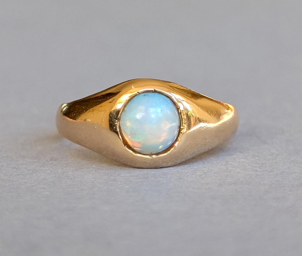 An antique yellow gold gypsy ring featuring a central round cabochon opal with blue and orange play-of-colour.
