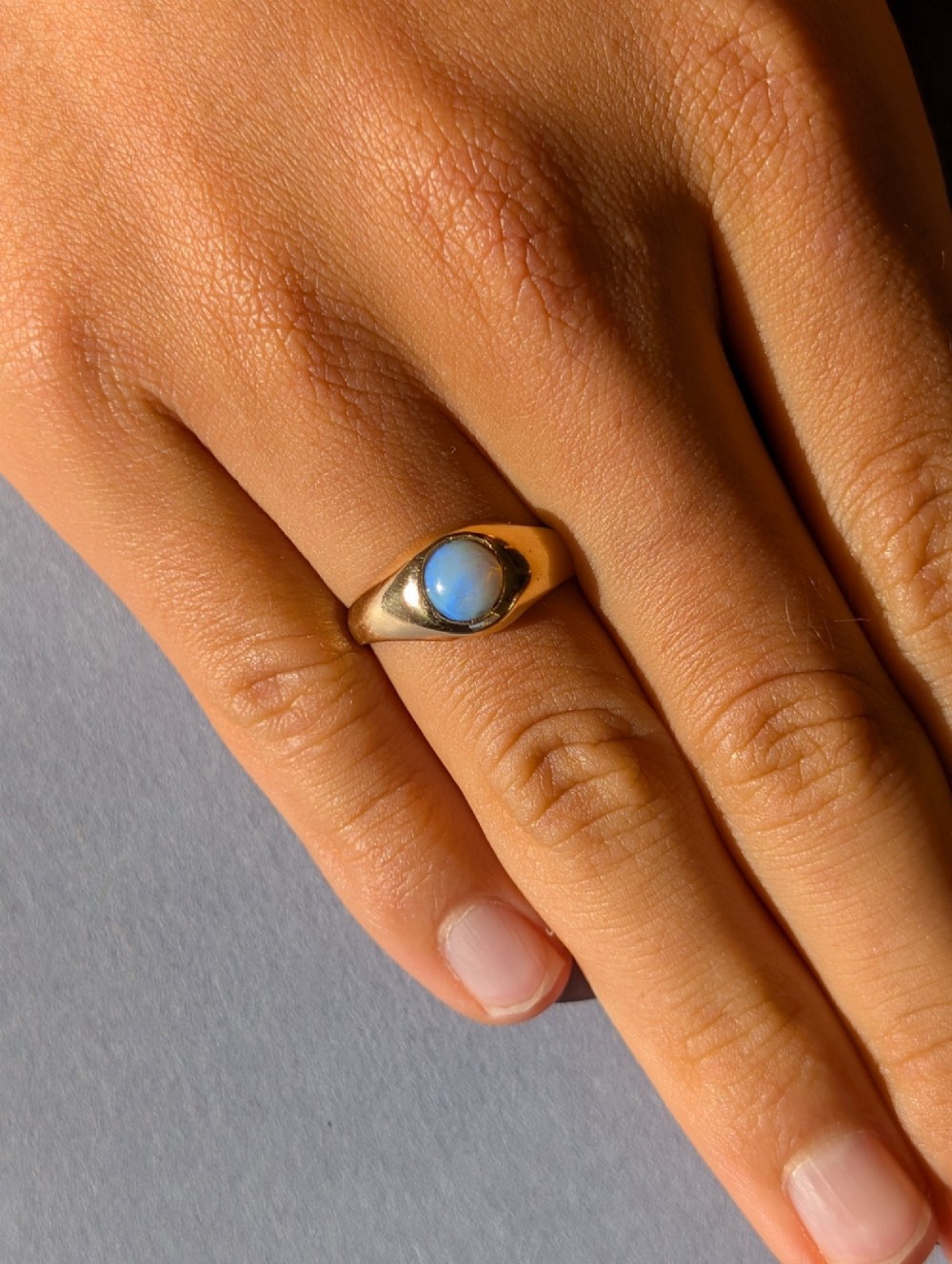 An antique yellow gold gypsy ring featuring a central round cabochon opal with blue and orange play-of-colour. View XV
