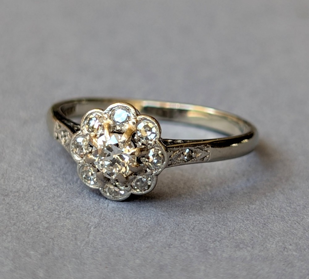 An Art Deco diamond cluster ring featuring a flower motif halo setting on a slender metallic band. View V