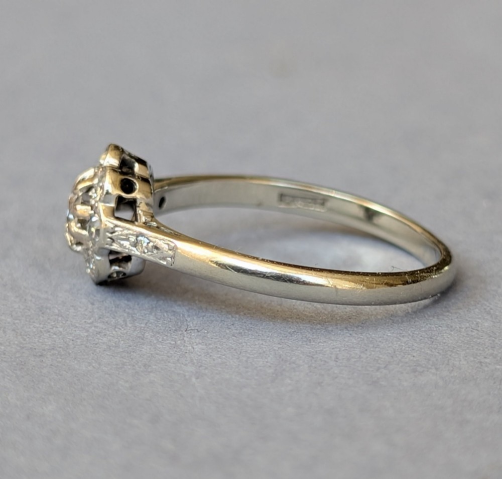 An Art Deco diamond cluster ring featuring a flower motif halo setting on a slender metallic band. View VII