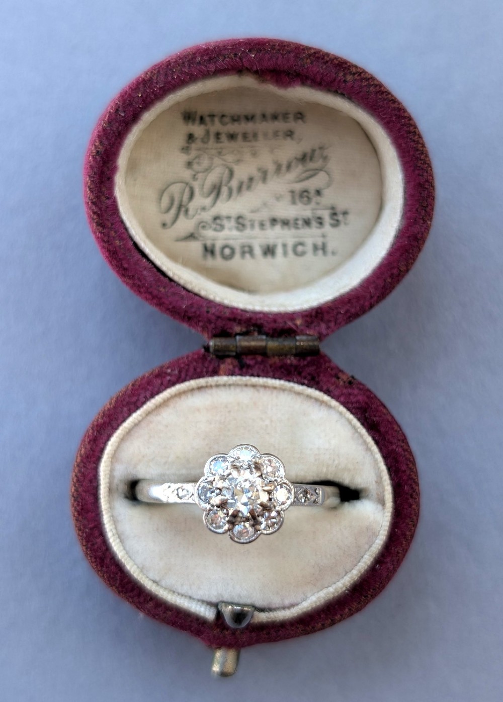 An Art Deco diamond cluster ring featuring a flower motif halo setting on a slender metallic band. View IX