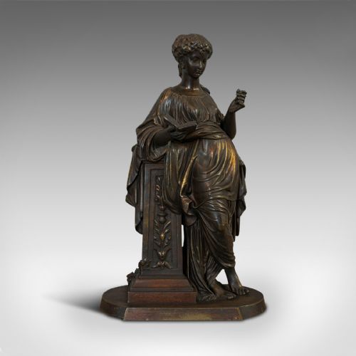 fig 1. An antique dark bronze figure depicting a draped female maiden holding a book and leaning against a carved pedestal.