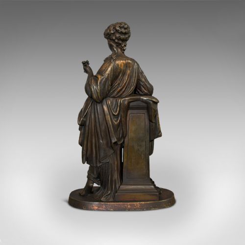 fig 5. An antique dark bronze figure depicting a draped female maiden holding a book and leaning against a carved pedestal.