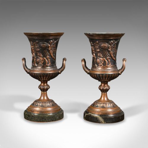 fig 1. A pair of patinated bronze urns featuring low-relief classical figures set upon dark circular marble bases.