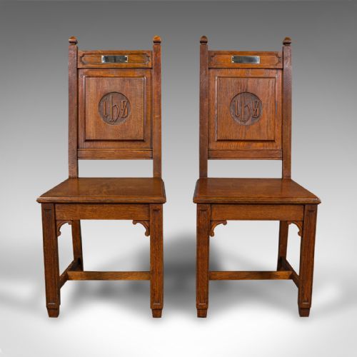 fig 1. A pair of antique Victorian English oak hall chairs featuring carved IHS monograms on the backrests and solid wooden seats.