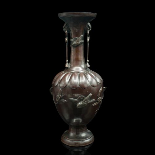 fig 1. A dark brown patinated bronze stem vase featuring high-relief carvings of birds among foliage, stylised mask handles with drop rings, and a fluted rim.