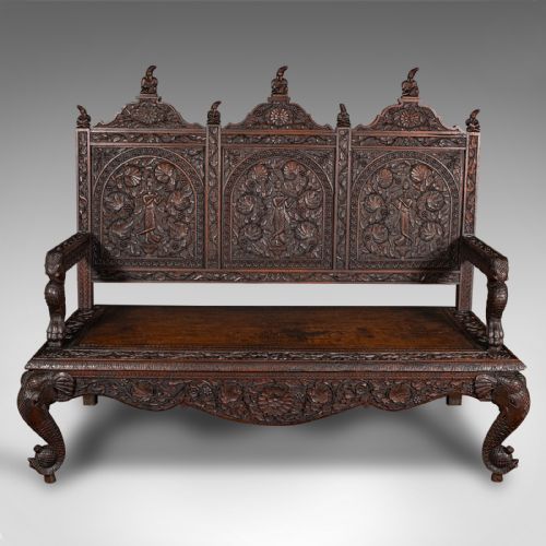 fig 1. A large dark teak three-seat bench featuring arched back panels with relief carvings, beast-form armrests, and carved legs.