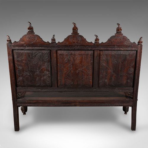 fig 3. A large dark teak three-seat bench featuring arched back panels with relief carvings, beast-form armrests, and carved legs.