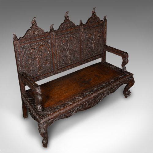 fig 4. A large dark teak three-seat bench featuring arched back panels with relief carvings, beast-form armrests, and carved legs.