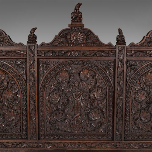 fig 6. A large dark teak three-seat bench featuring arched back panels with relief carvings, beast-form armrests, and carved legs.