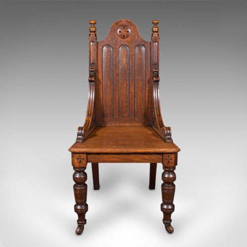 fig 1. A Victorian Scottish oak Gothic Revival hall chair featuring a carved arched back, turned front legs on castors, and cross motifs on the frame.