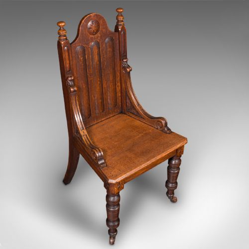 fig 3. A Victorian Scottish oak Gothic Revival hall chair featuring a carved arched back, turned front legs on castors, and cross motifs on the frame.