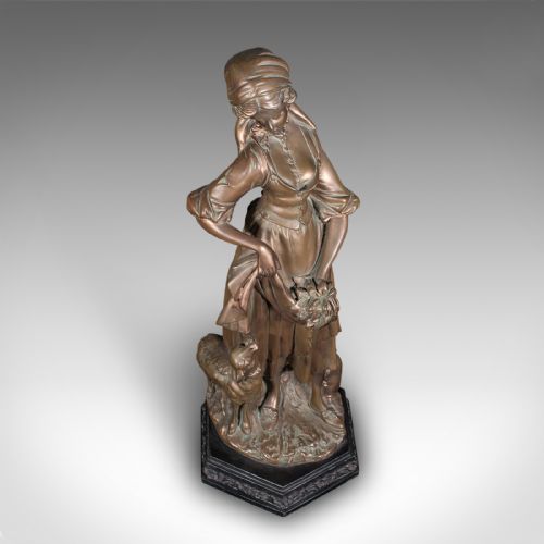 fig 4. An antique bronzed plaster statue depicting a standing woman in rustic attire holding a basket alongside a small dog on a dark octagonal plinth.