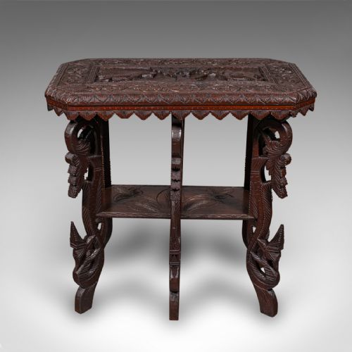 fig 1. A dark brown hand-carved teak occasional table featuring animal relief carving on top, pierced foliage legs, and a lower shelf tier.