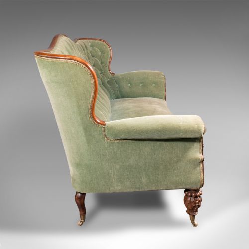 fig 3. An antique seven-foot wide English settee featuring sage green velvet button-back upholstery, a carved walnut frame, and scrolled legs on brass castors.