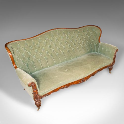 fig 4. An antique seven-foot wide English settee featuring sage green velvet button-back upholstery, a carved walnut frame, and scrolled legs on brass castors.