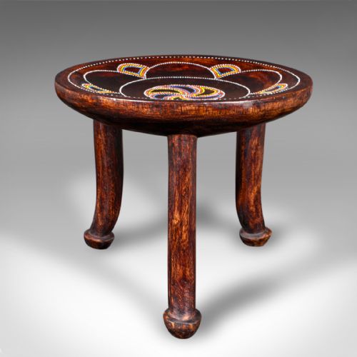 fig 3. A low circular dark fruitwood side table or stool supported by three splayed legs, decorated with colorful beaded swirl patterns across the top.