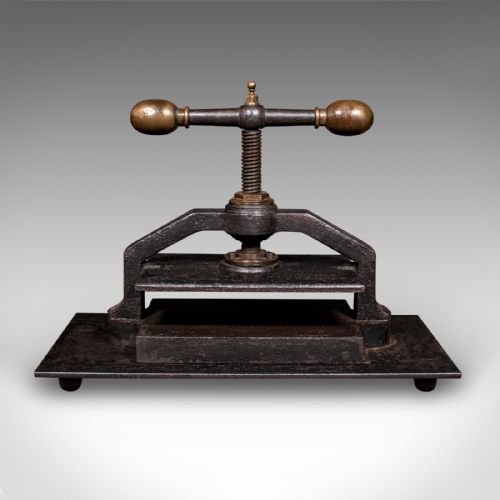 fig 1. A dark cast iron book press featuring a central threaded screw, brass handle knobs, and a rectangular base plate.