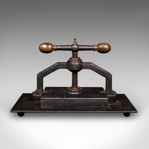 fig 2. A dark cast iron book press featuring a central threaded screw, brass handle knobs, and a rectangular base plate.