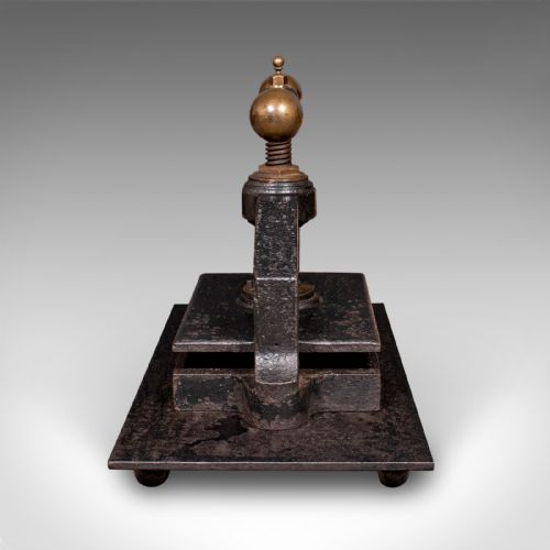 fig 3. A dark cast iron book press featuring a central threaded screw, brass handle knobs, and a rectangular base plate.