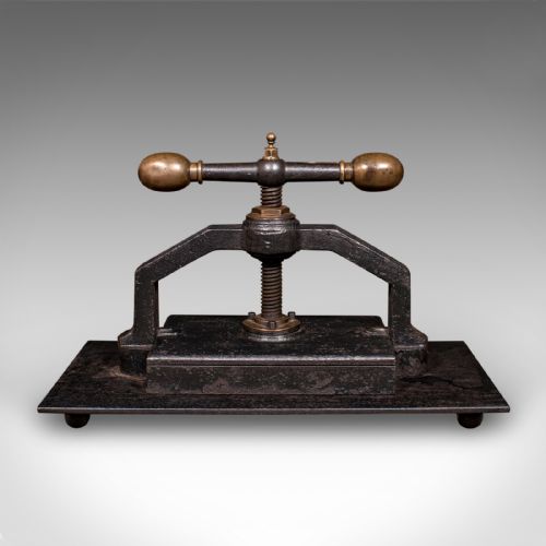 fig 4. A dark cast iron book press featuring a central threaded screw, brass handle knobs, and a rectangular base plate.